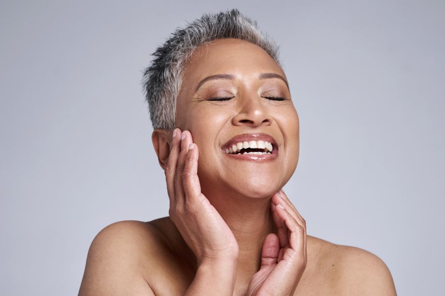 woman with short grey hair, eyes closed with big smile